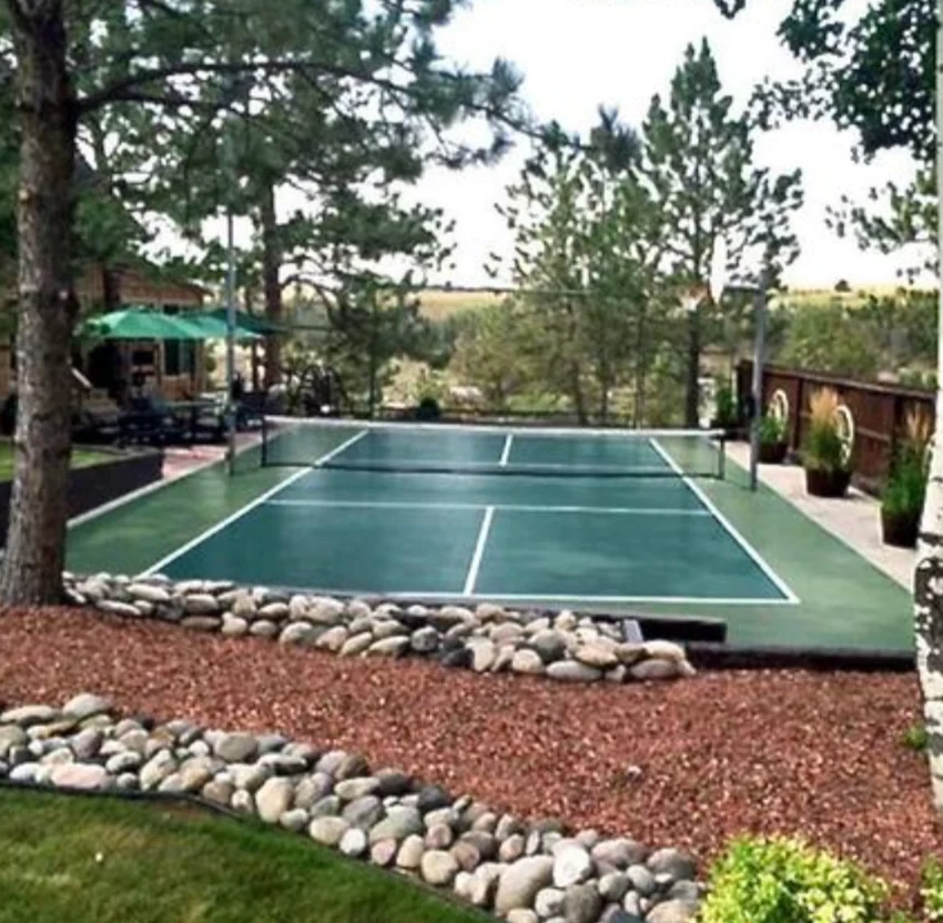 Blue and gray backyard pickleball court beneath mature trees